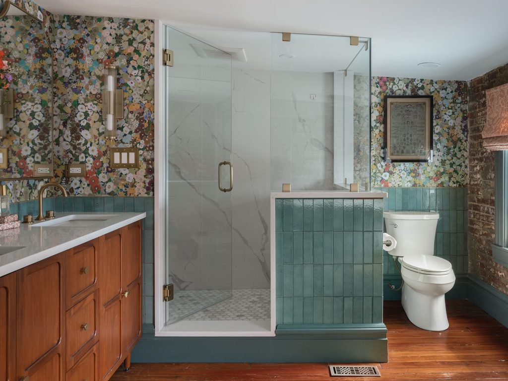 Glass shower with aqua-tiled half wall, teal baseboards, original wood floors, and exposed brick in a St. Louis bathroom