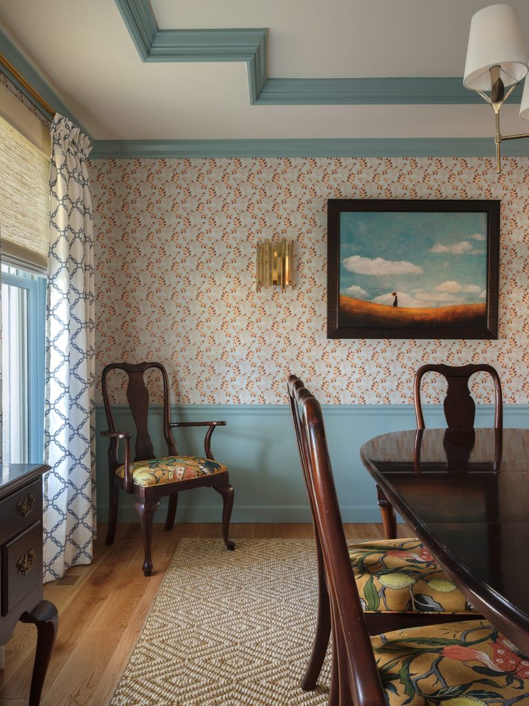 Dining room corner with blue lattice embroidered curtains, two-tone walls, and a brass sconce