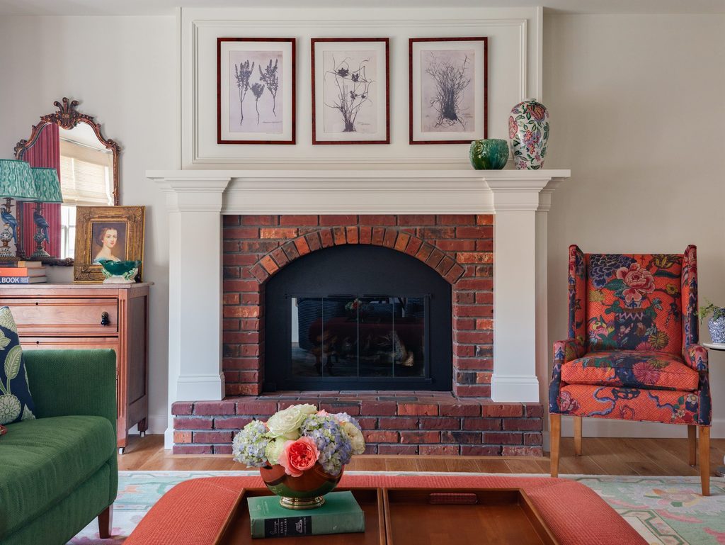 Brick fireplace clad in a custom white mantel and paneled overmantel with three framed botanical prints