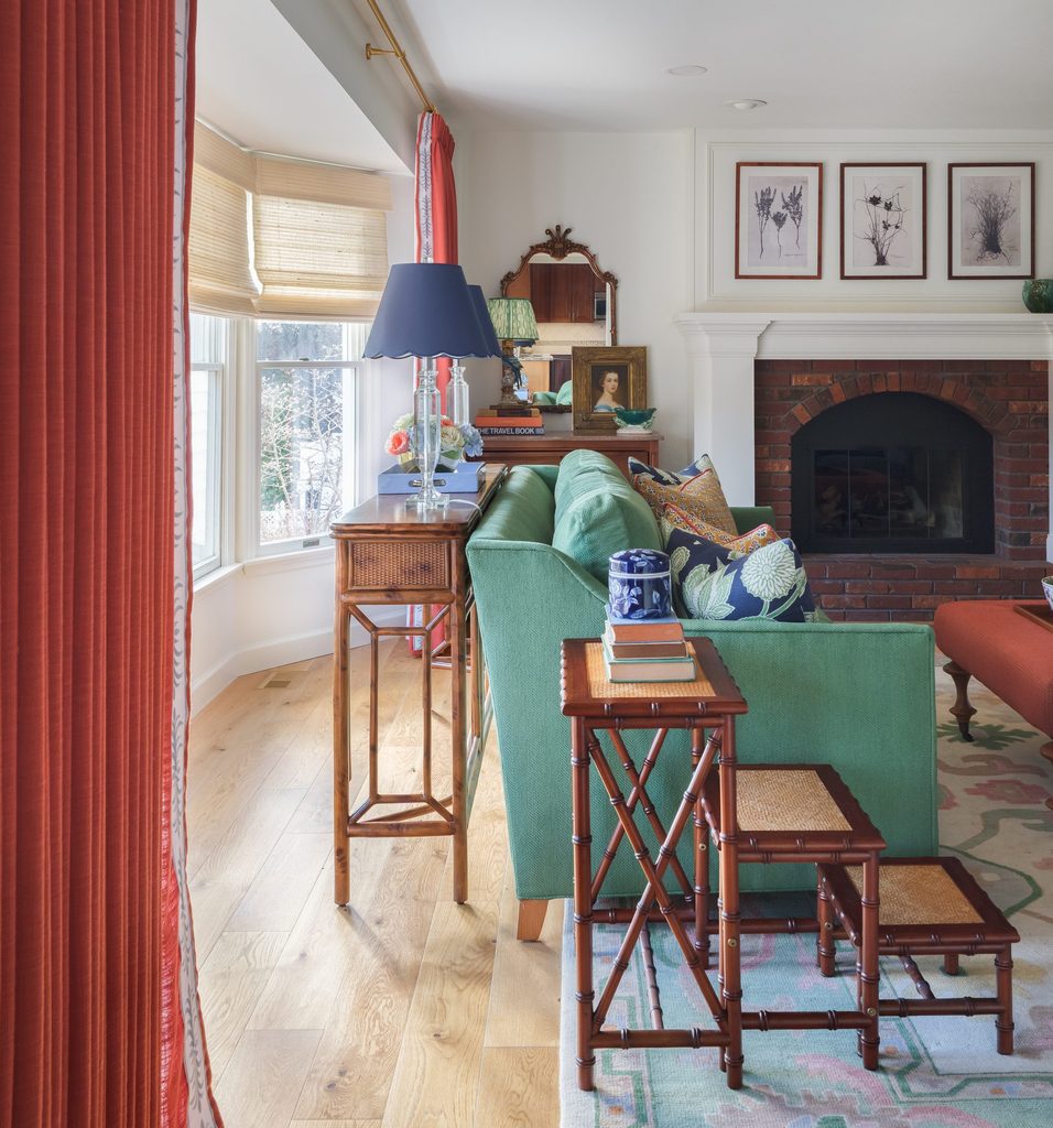 Green sofa with a faux bamboo console, navy scalloped lamps, and nesting tables in a colorful family room
