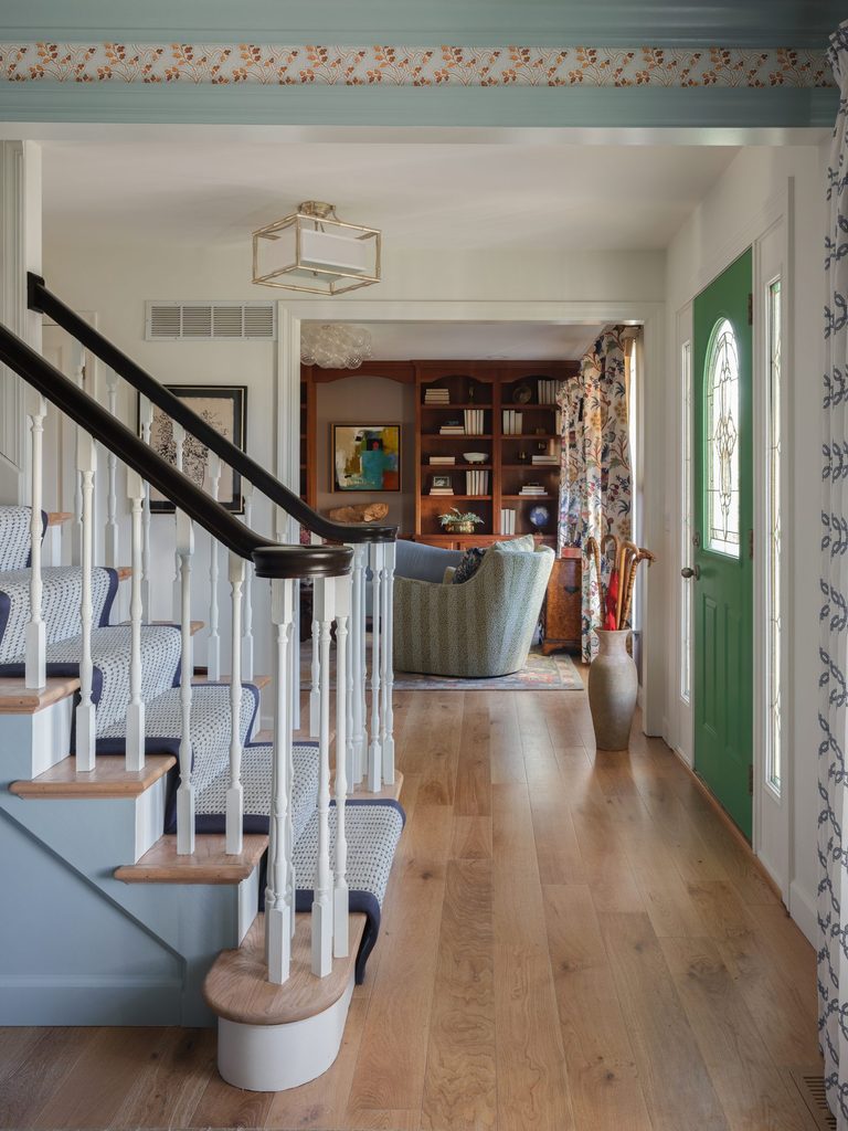 Foyer with a green front door, navy-bordered stair runner, and a view into the sitting room