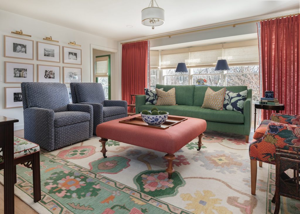 St. Charles interior design family room with a kelly green sofa, coral ottoman, coral curtains, and a lit gallery wall of family photos