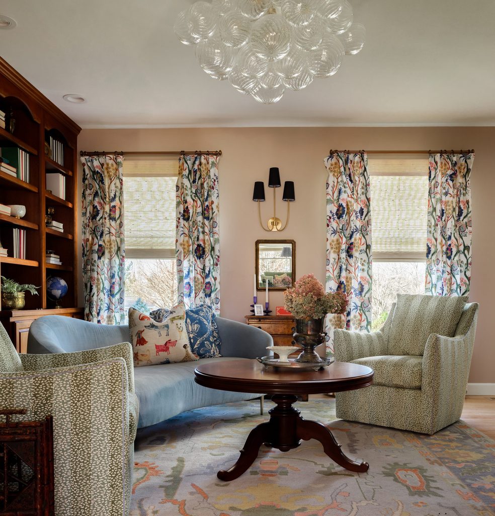 St. Charles sitting room with a curved blue velvet sofa, green chairs, heirloom coffee table, and floral curtains